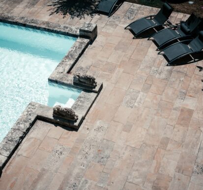 Elegant stone patio and courtyard design with poolside loungers and decorative stone features, showcasing modern outdoor living spaces.